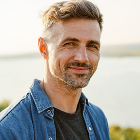 Man in a denim shirt smiling outdoors