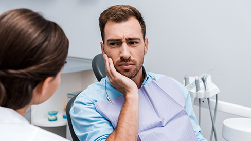 Man holding his cheek in pain while talking to his emergency dentist
