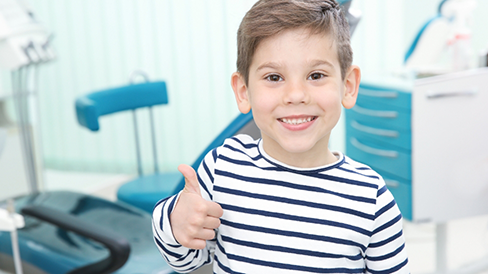 Child in a dental office smiling and giving a thumbs up
