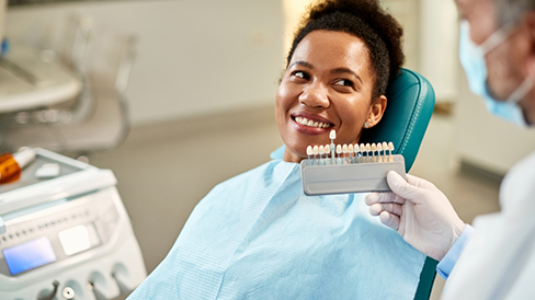 Dentist holding a row of veneers in front of a smiling patient