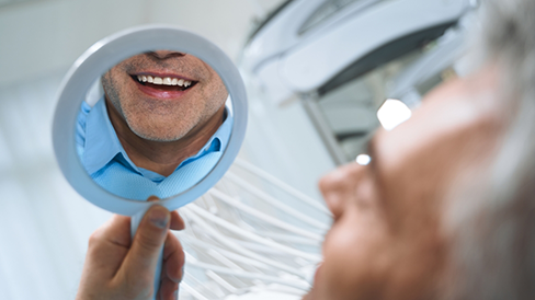 Dental patient looking admiring his new smile in a mirror