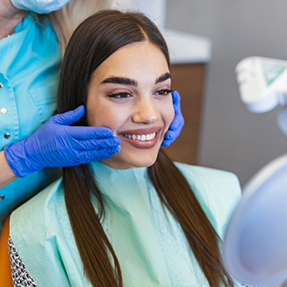 Young woman in the dental chair admiring her smile in a mirror
