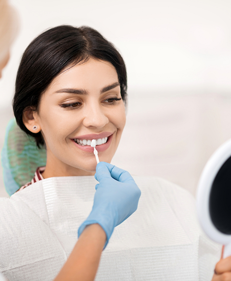 Woman smiling as a dentist holds a veneer in front of her tooth