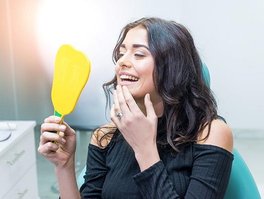 Woman in dentist’s chair looking in hand mirror