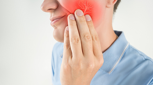 Person wincing in pain and touching their cheek